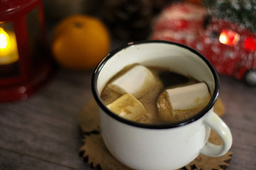 Coffee with marshmallow in a white cup on a blurred wooden background. In frame view a red lantern, mandarins. Holiday concept