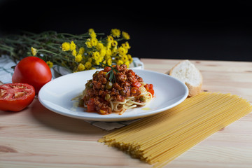 Italian spaghetti with a meat based sauce in a plain white plate on wooden table. Spaghetti pasta with tomatoes.