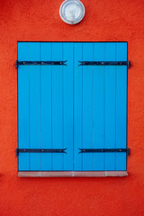 Blue wooden closed shutters on window against orange wall