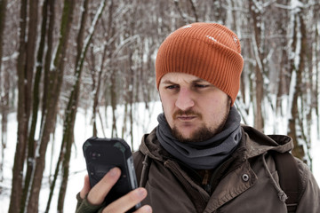 Fototapeta na wymiar a man uses a mobile phone in a snowy forest. Mobile networks. Addiction. Call for help. Call rescue. battery discharge and signal loss, smartphone for tourism and trips. Serious look
