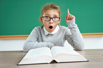 Curious schoolgirl reads book. Photo of astonished little girl wearing glasses, pointing finger up....