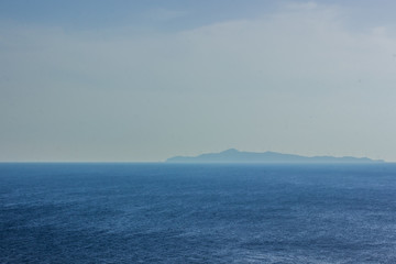 Fototapeta premium open sea nature scenery landscape and unfocused big island on horizon line background in morning sun rise foggy weather time, south wallpaper pattern concept with empty space for copy or text