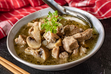 Soup with pieces of pork and mushrooms in bowl.