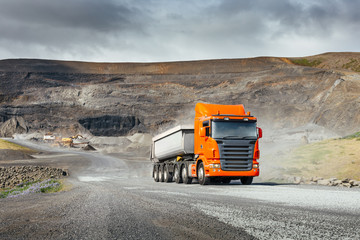 Modern orange european truck with white heavy duty dump trailer drives after load from quarry in a...