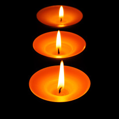 Drei brennende Teelichter vor schwarzem Hintergrund