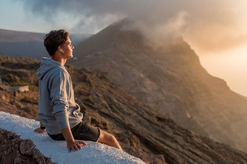 Naklejka premium Young handsome guy enjoying of beautiful landscape view, sitting on the roadside on the mountain hill.