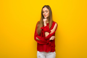 Young girl with red dress over yellow wall looking down with the hand on the chin