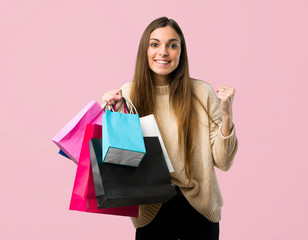 Young girl with shopping bags celebrating a victory in winner position on isolated pink background