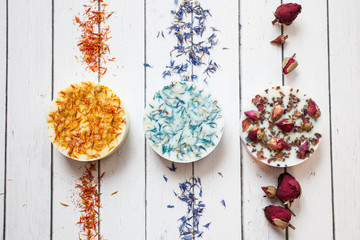 collection of handmade soap with dried flowers of rose, cornflower and calendula on a white wooden background