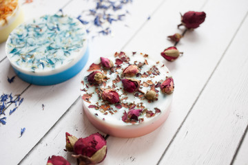 cropped photo round piece of handmade soap with dried flowers of a rose on a white wooden background