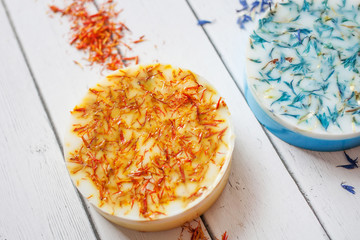 cropped photo of a round piece of handmade soap with orange dried flowers of calendula on a white wooden background