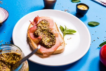 Sandwich with ham and mustard on a white ceramic plate, blue background