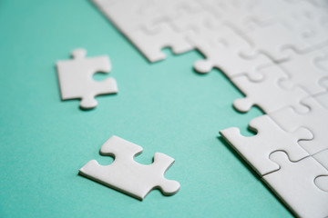 Fragment of a folded white jigsaw puzzle and a pile of uncombed puzzle elements against the background of a colored surface.