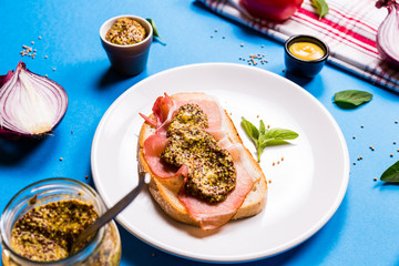 Sandwich with ham and mustard on a white ceramic plate, blue background
