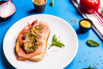 Sandwich with ham and mustard on a white ceramic plate, blue background