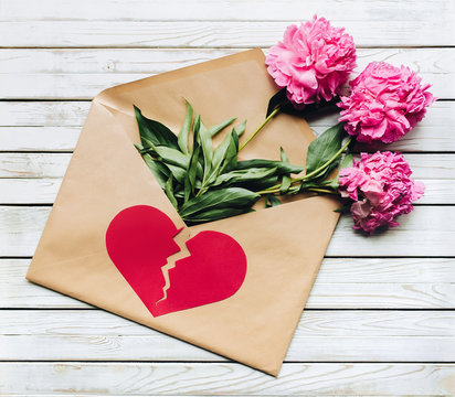 Three fade purple peonies lay in open brown kraft envelope containing. Symbol of unhappy love in the form of a broken heart. The concept of breaking relationships. Marriage proposal.