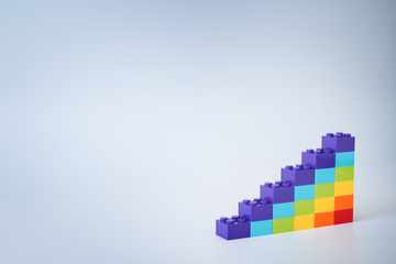Colorful rainbow colored ascending stacks made of toy building bricks on gray background. Copy space.