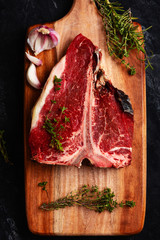T bone of beef with spices on a wooden board and black background. Raw dry aging steak 3 months.