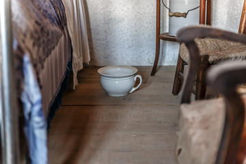 Old white urinal placed next to a bed in a bedroom in a house