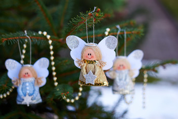 Christmas angels on a branch of a Christmas tree and golden beads. Handmade holiday decorations. New Year's toy. Natural photo on the street. Snowy weather. Winter vacation. 