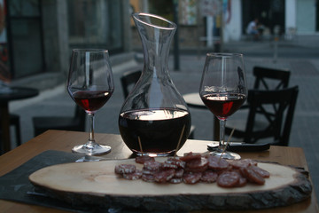 Two red wine glasses, a wine decanter and a salami platter