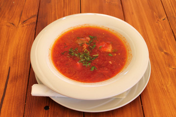 A dinner plate with beetroot soup (borsch) on a wooden table