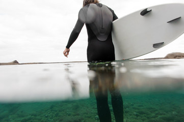 Naklejka premium Guy standing in the black swimsuit with a surf in his hands in the sea water