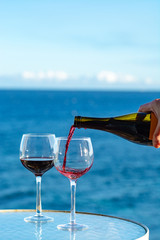 Waiter pouring aperitif red wine in glasses on outdoor tessace witn sea view