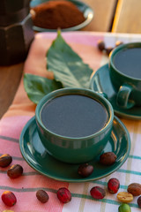 Obraz na płótnie Canvas Cup with black coffee served outside with raw green, mature red and roasted coffee beans, decorated with green leaves from coffee plant