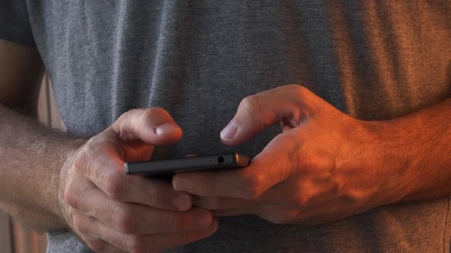 Guy is typing text message on his smartphone device, close up of hands using thumbs for texting