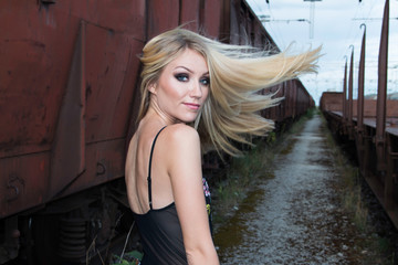 Beautiful blonde girl walking on rail tracks, romantic look, from back, wind in the hair, fashion...