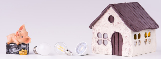 Led lamps and piggy bank lie near the house layout on a white background. Theme energy saving in the house    
