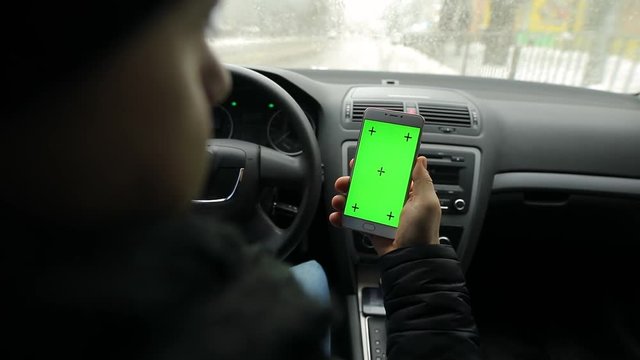 Man using empty green screen of smartphone in car, chroma key