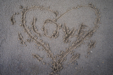Heart is drawn in the sand of a beach by a stick in the center of the inscription love.