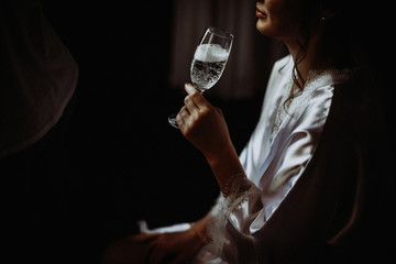 bride in bathrobe holds a glass of champagne in hand in the morning