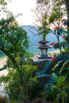 Green shore of lake Fewa, Pokhara. Small hindu temple and flowering trees.