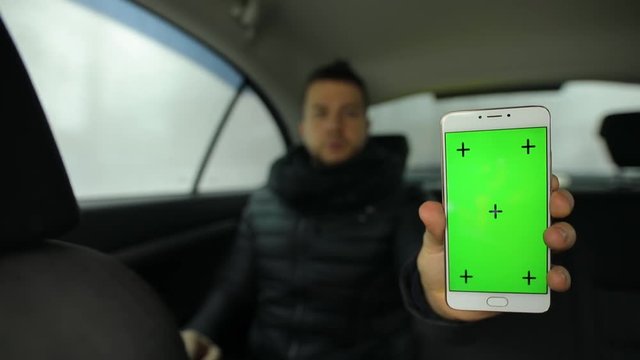 Man demonstrating empty green screen of smartphone in car salon, chroma key