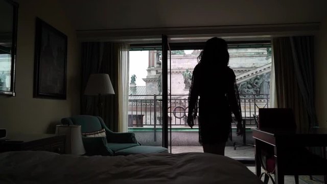 Young sexy brunette woman in lingerie in bedroom going to balcony. Flirting of lovely female in hotel room. Slowmotion. Walking to to window silhouette