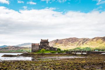 Eilean Donan Castle in the Highlands of Scotland on a cloudy day and low tide, ancient castle with sandstone bridge, lush nature with colorful moss and lichens 