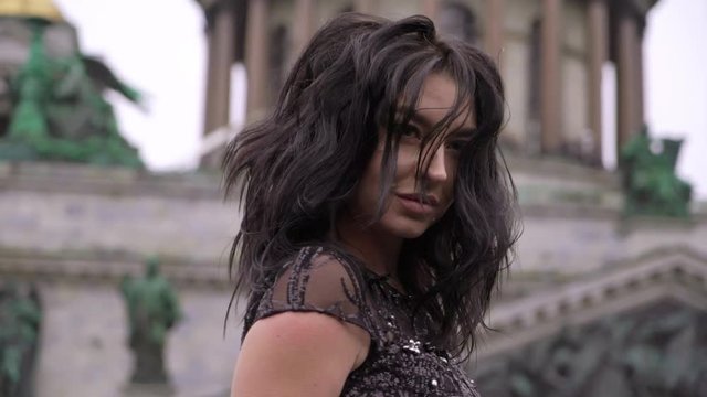 Young sexy brunette woman in black luxury dress staying at balcony in a city. Flirting or lovely female in hotel. Slowmotion.