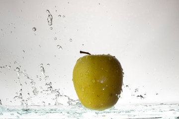 Fototapeta na wymiar Green apple on a light background and splashing water