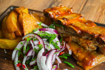 A grilled pork and fried potatoes on the wooden background.
