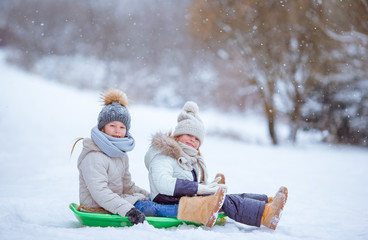 Adorable little happy girls sledding in winter snowy day.