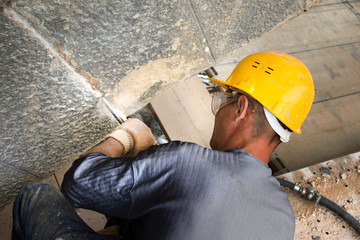 Worker remove old grout between stone blocks with air hammer