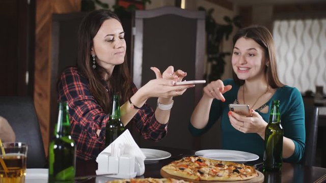 The company of cheerful girls in the restaurant. Girls having fun drinking beer and eating pizza. Girls pictures of pizza on your smartphone.