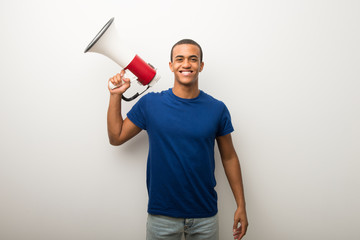 Young african american man on white wall holding a megaphone