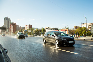 Driving in big city. Drive tuning car in rain on asphalt wet road. Clouds and sun.