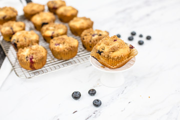 homemade blueberry muffins on wire rack on white and gray marble countertop; one isolated in front