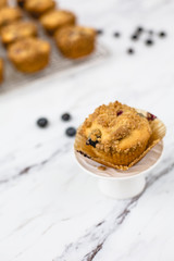 homemade blueberry muffins on wire rack on white and gray marble countertop; one isolated in front