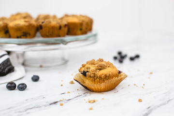 homemade blueberry muffins on cake pedestal on white and gray marble countertop; one isolated in front